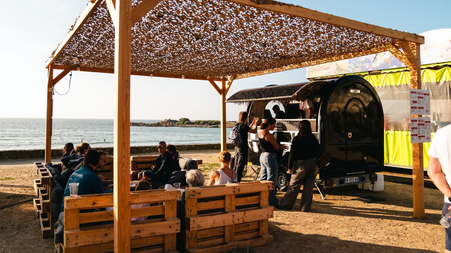 Remorque food truck en bord de plage, clients attablés sous la pergola